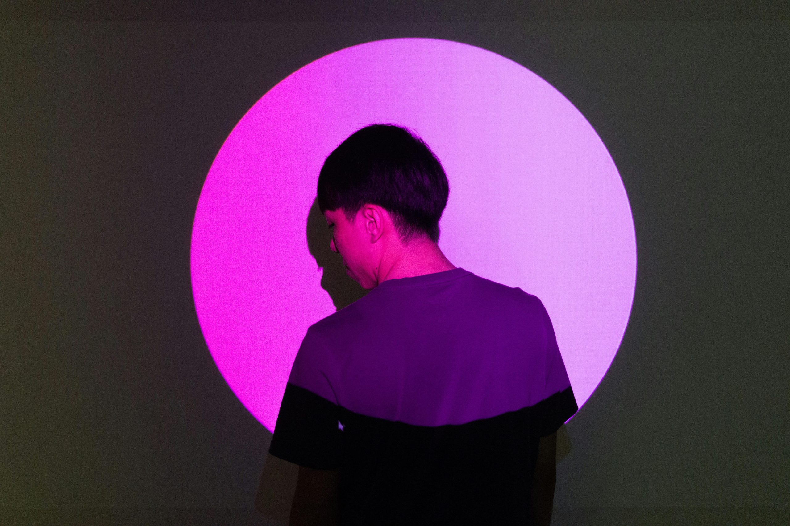 A person stands in front of a bright pink circular light, creating a striking silhouette effect.